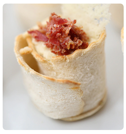 An appetising food close-up with a bacon roll in sharp focus in the foreground while the background is in soft focus.